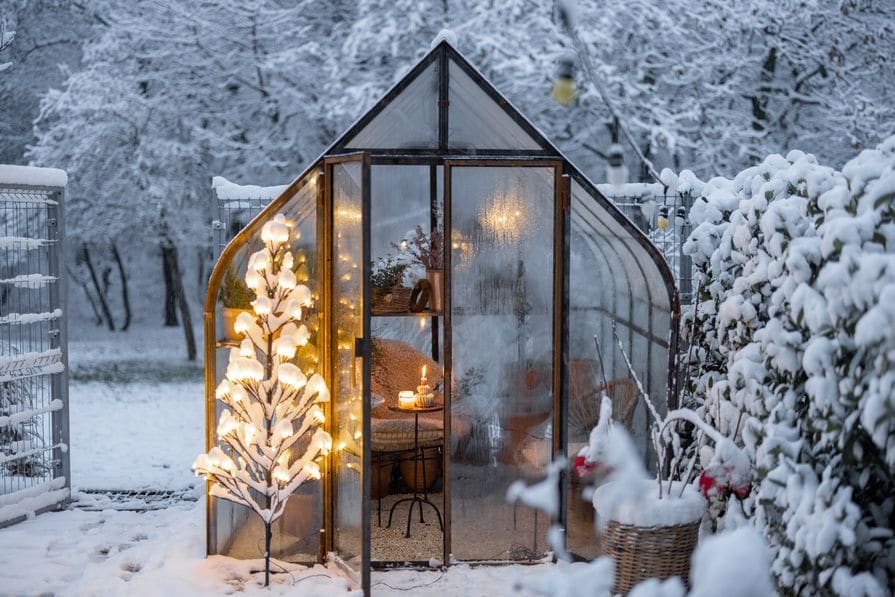 Weihnachtlich geschmücktes Gewächshaus in einem verschneiten Garten